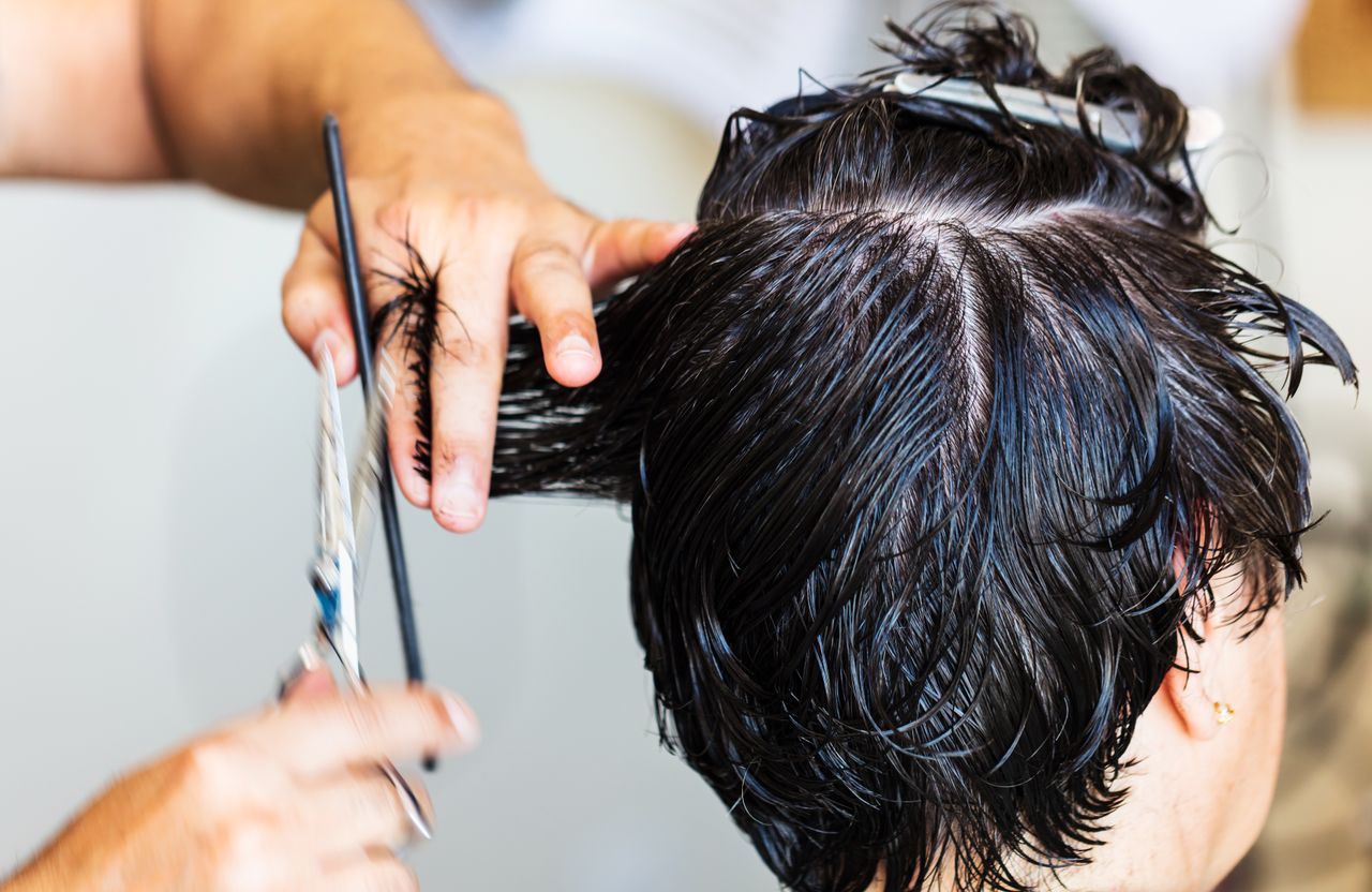 our-story-01 Close-up of a stylist cutting dark, wet hair in a salon setting, showcasing the precision and technique of hairstyling.