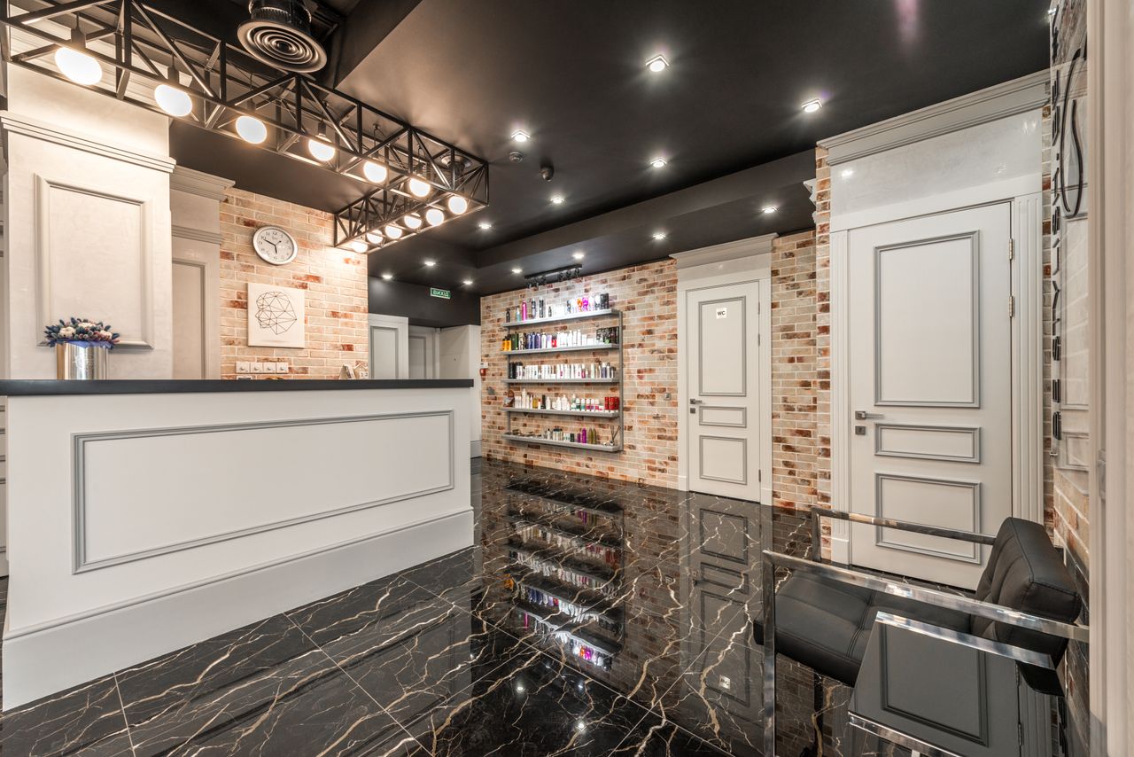 mission-02 White reception counter with flowers placed in stylish beauty salon with doors and shelves with various cosmetology supplies at brick wall